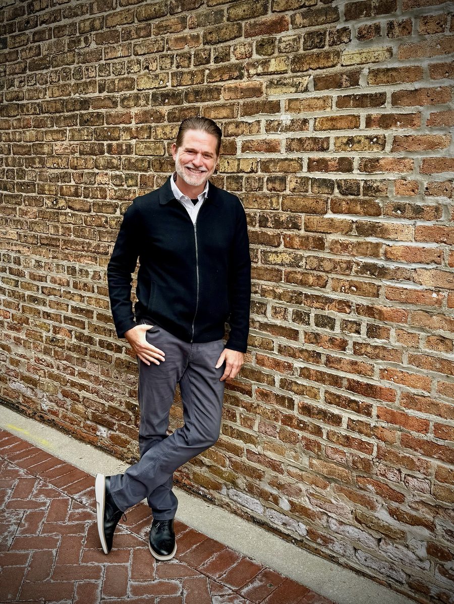 Billy Hyland leaning against a brick wall, holding a copy of The What If Shift