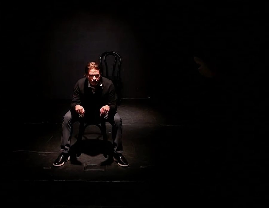 Billy Hyland seated on stage under a spotlight, mid-speaking engagement
